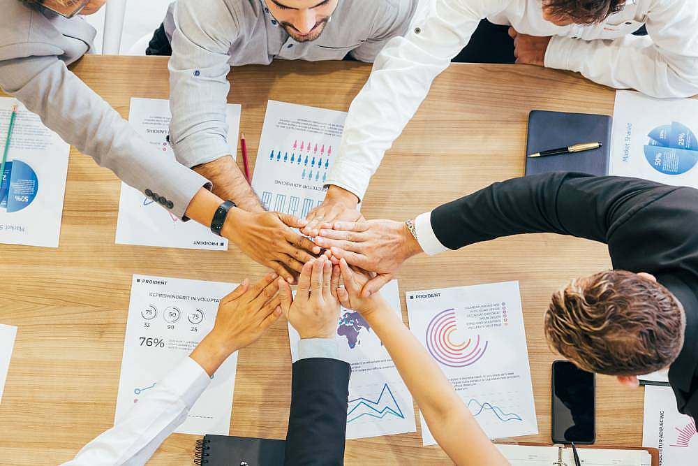Team of professionals stacking hands over a table with business reports and charts.