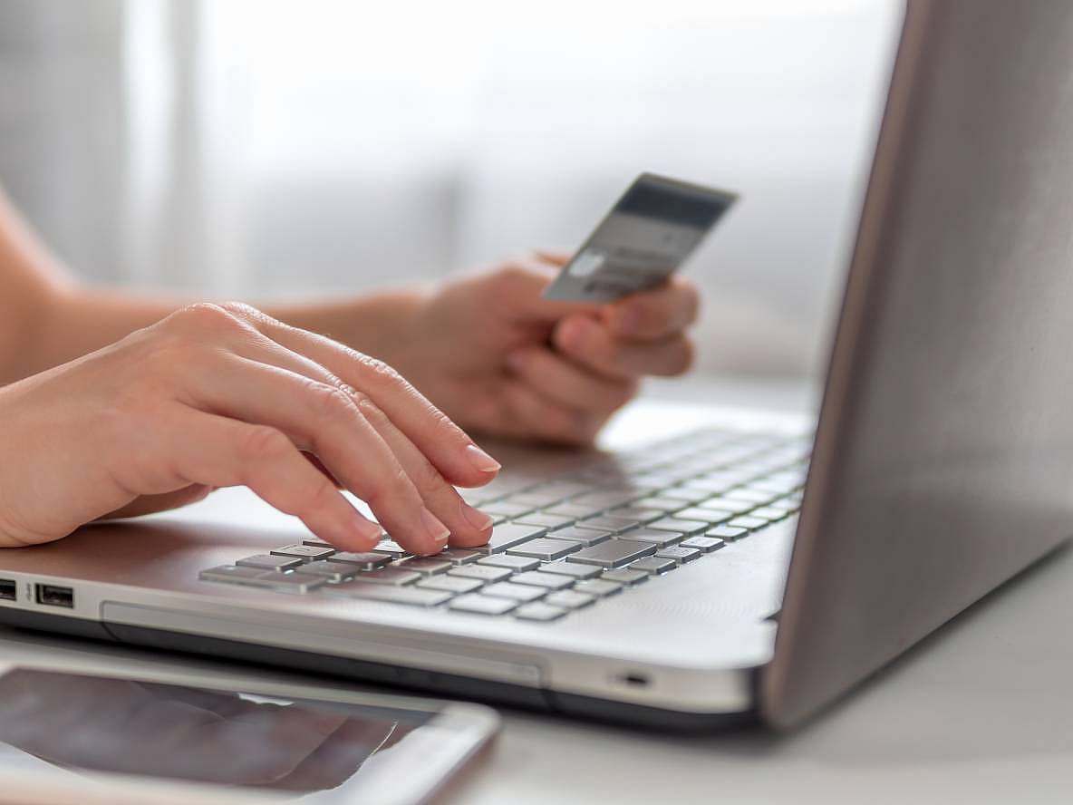 Person holding a credit card while typing on a laptop keyboard, suggesting online shopping or online banking activity.